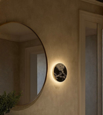 Soft warm backlit marble round wall lamp mounted near a large mirror in a contemporary hallway.