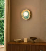 Organic ring wall sconce with glowing central globe mounted on a warm modern interior wall