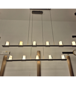 Modern black linear 6-light pendant chandelier with warm white diffusers suspended above a luxury kitchen island.