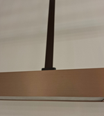 Modern triple linear LED pendant light with champagne-toned rectangular light modules and black adjustable suspension above a contemporary dining table.