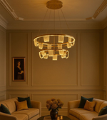 Ophelia Gold chandelier glowing warmly above beige sofas in a luxury sitting room.