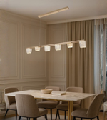 Straight bar acrylic chandelier with warm LED light above a wooden dining table