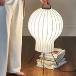 Soft white paper lantern floor lamp with tripod stand beside books