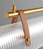 Glass pendant light fixture with gold rod and brown leather strap on a gray background