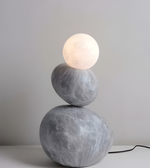 Modern lamp with stacked stone-like bases and a round light bulb on a neutral background