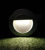 Round ground light emitting a bright white glow on grass with a dark background