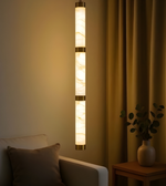 Wall-mounted cylindrical light fixture in a room with a couch and plant.