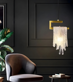Modern chandelier hanging in a dark room with a chair and plant.