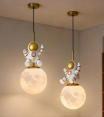 Two hanging pendant lights with astronaut figures on a neutral wall background