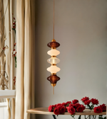 Modern pendant light fixture with red roses on a wooden shelf against a neutral wall.