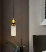Modern pendant light with gold fixture and white glass shade hanging in a room.