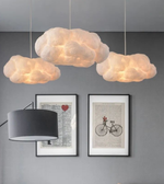 Cloud-shaped pendant lights hanging above a wall with framed pictures and a lamp.