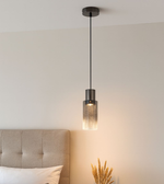 Modern smoked glass cylinder pendant light hanging beside bed creating warm ambient lighting in contemporary bedroom