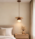 scandinavian wood pendant light with round disc and frosted globe hanging beside bed, warm ambient bedroom lighting
