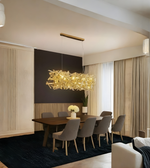 Modern dining room with a gold chandelier, wooden table, and gray chairs.