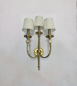 Brass wall sconce with three white lampshades on a light gray background