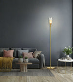 A modern gold floor lamp with a sculptural white leaf-shaped shade stands in a styled living room next to a gray sofa and a small white side table.