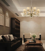 A modern living room featuring a multi-light chandelier with cream drum shades and brass arms hanging over a dark leather sofa and wooden coffee table.