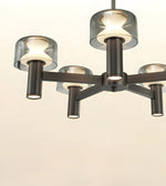 A modern 5-light chandelier with a dark gunmetal metal frame and translucent smoky glass shades, shown illuminated against a plain off-white background.