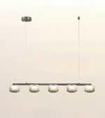 A modern 5-light linear pendant chandelier with clear glass cylindrical shades and a dark metal frame, suspended from a ceiling canopy against a light beige background.