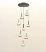 A modern multi-light chandelier pendant fixture with a circular dark metal canopy, multiple hanging cords, and cylindrical frosted glass shades glowing with warm light, shown against a plain light background.