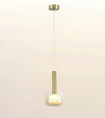 A modern single pendant light with a brushed gold metal cylinder stem and a frosted white glass shade, suspended by a thin cord against a warm off-white background.