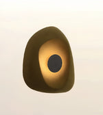 An abstract organic-shaped wall sconce or light fixture with a dark brown outer shell and a glowing warm gold center, set against a soft off-white background.