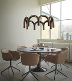 A modern dining room scene featuring a unique bronze-toned pendant light with curved arches hanging over a round black table surrounded by six beige armchairs.