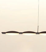 A modern linear pendant light with three illuminated oval frosted shades and a dark metal frame, suspended by a thin cord against a plain off-white background.