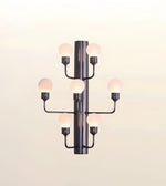 A modern multi-light wall sconce with a matte black central column and six curved arms, each holding a glowing frosted globe bulb, shown against a plain light background.