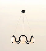 A modern multi-light pendant chandelier with a black wavy metal frame and five glowing white spherical glass shades, suspended from a ceiling canopy against a plain light background.