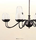 A multi-arm chandelier with a dark bronze metal frame and textured clear glass shades, shown against a plain beige background.