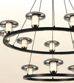 Modern multi-tier ring chandelier with brushed silver metal circular frames, black suspension rods, and glowing warm white glass shades.