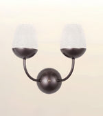 A modern two-light wall sconce with a matte dark bronze finish and textured white glass shades, shown against a soft beige gradient background.