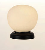 A table lamp with a large, rounded, frosted off-white glass globe shade on a round, dark brown wooden base, set against a plain light background.