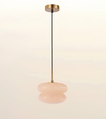 A modern pendant light with a brushed brass ceiling canopy and downrod, a black cord, and a double-tiered, rounded blush pink glass shade, shown against a warm off-white background.