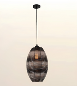 A hanging pendant light with a dark metal frame and a warm glowing bulb inside, suspended against a plain light background.
