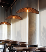 Three woven wicker pendant lights with warm glowing bulbs hanging over a dining area with wooden tables and chairs.