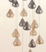 A modern multi-light chandelier featuring multiple teardrop-shaped glass pendant shades in smoked silver and warm champagne beige, suspended by thin cables against a solid off-white background.