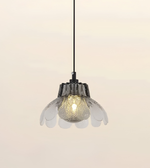 A modern pendant light with a black hanging cord and a flower-shaped clear glass shade, shown illuminated against a soft beige background.