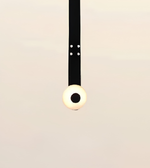 A minimalist pendant light with a black cord and a spherical bulb that glows warm white, suspended against a plain light beige background.