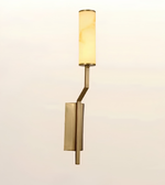 A modern wall-mounted sconce light fixture with a cylindrical warm white glass shade and a brushed brass or gold-toned metal body, shown against a plain light background.