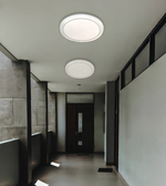 Two round flush-mount ceiling light fixtures installed on a white ceiling in a modern hallway with gray tiled walls and a dark wooden door.