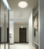A modern ceiling light fixture with a circular white glass shade and a decorative textured silver-toned outer rim, shown installed in a contemporary hallway with white walls and a dark wood door.