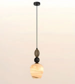 A modern pendant light with a black metal canopy and cord, featuring a smoky glass decorative bead, a black sphere accent, and a warm marbled amber glass shade, shown against a soft beige gradient background.