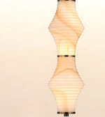 A modern pendant light with a sculptural, ribbed glass shade featuring a twisted spiral design and a warm glowing light, shown against a soft beige background.