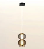 A modern pendant light fixture with two stacked textured glass shades in a warm metallic finish, suspended by a slim black cord from a matching black ceiling canopy against a soft beige gradient background.