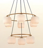 A modern multi-light chandelier with five ribbed glass cylindrical shades and a gold-toned circular metal frame, suspended by black cords against a plain off-white background.