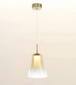 A modern pendant light with a clear glass bell-shaped shade, a warm glowing bulb inside, and a brushed brass metal canopy and rod, suspended against a plain off-white background.