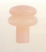 A translucent peach-colored silicone or rubber cap with a rounded, tiered design and a cylindrical base, shown against a solid off-white background.